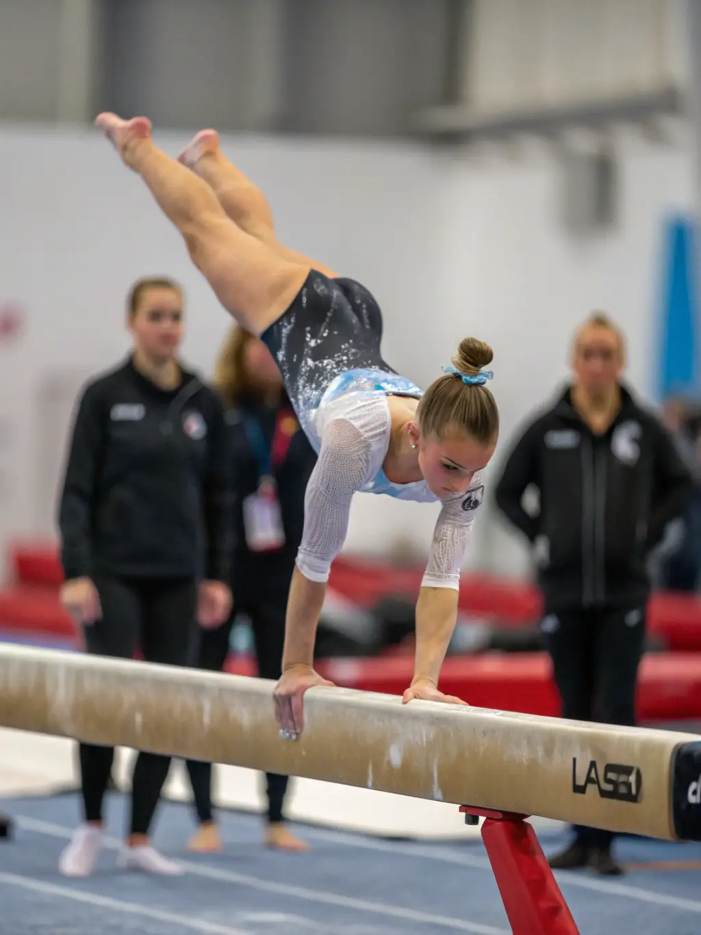 Teenagers practicing advanced gymnastics routines on the balance beam, showcasing their skill and precision under the guidance of a coach at GYMNAST VOLONT AURILLAC NORD.